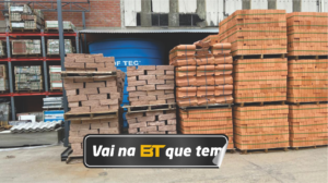 Tijolos e pedras gres (usadas no alicerce) empilhados em um amplo galpão, com outros itens de construção ao fundo. Estoque da empresa.